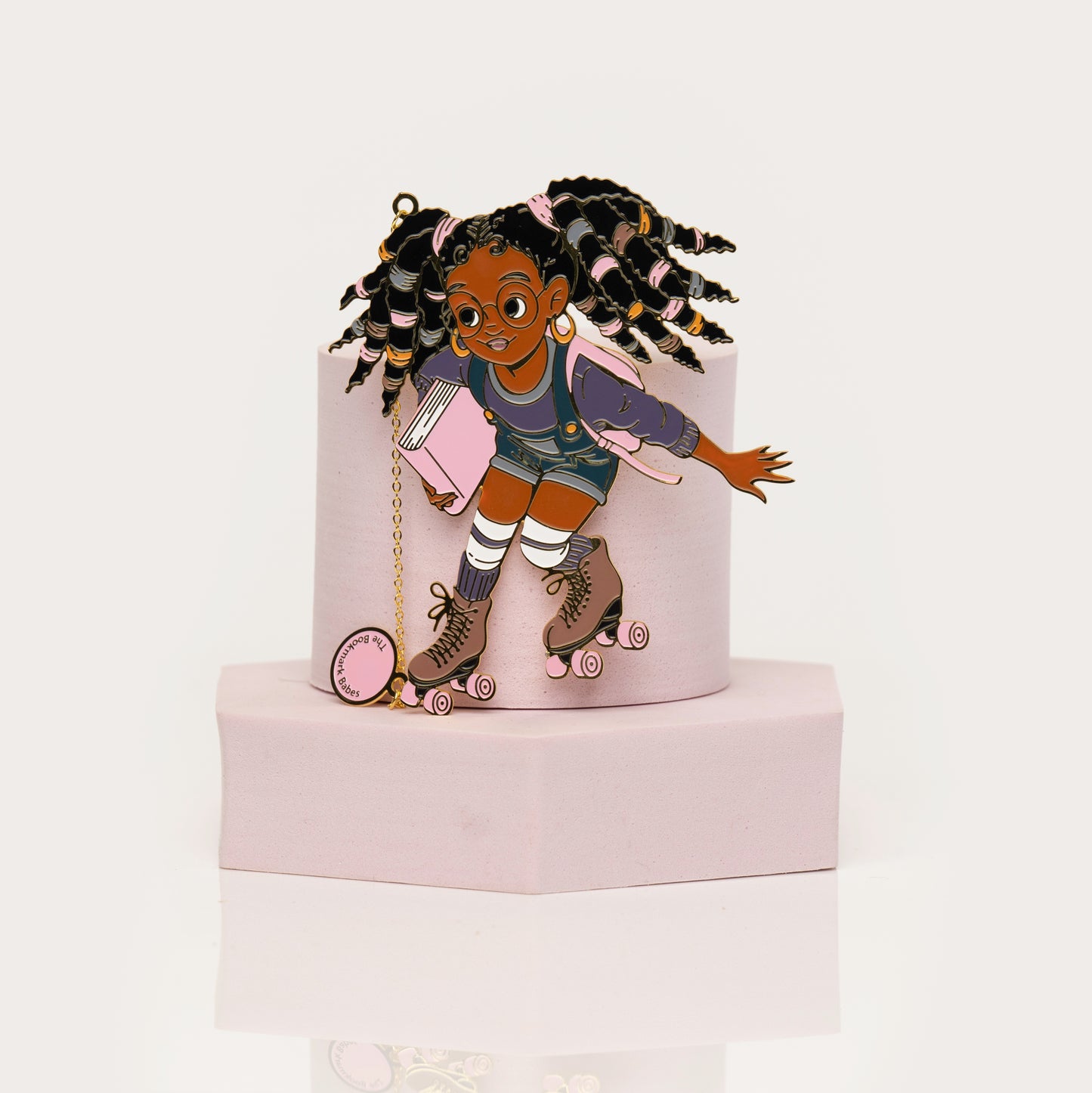 Enamel bookmark of Black girl on rollerskates with locs holding a book