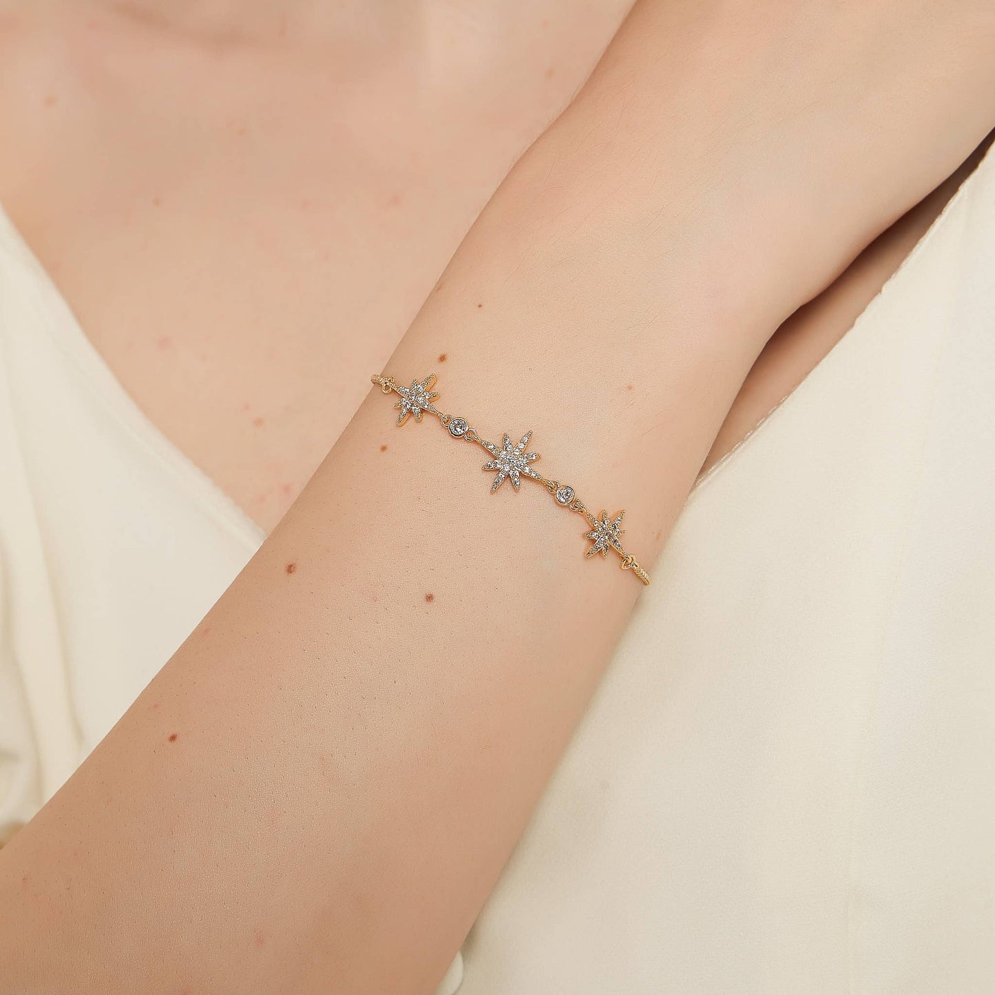 Gold celestial bracelet with starburst details and cubic zirconia accents, styled on wrist with a minimal, delicate aesthetic.