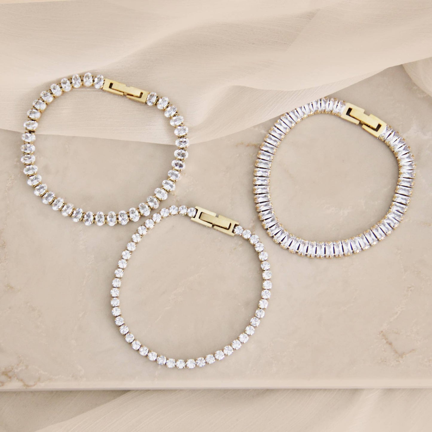 Minimal CZ tennis bracelet in gold over surgical steel, featuring a refined, understated design styled on a neutral marble surface.