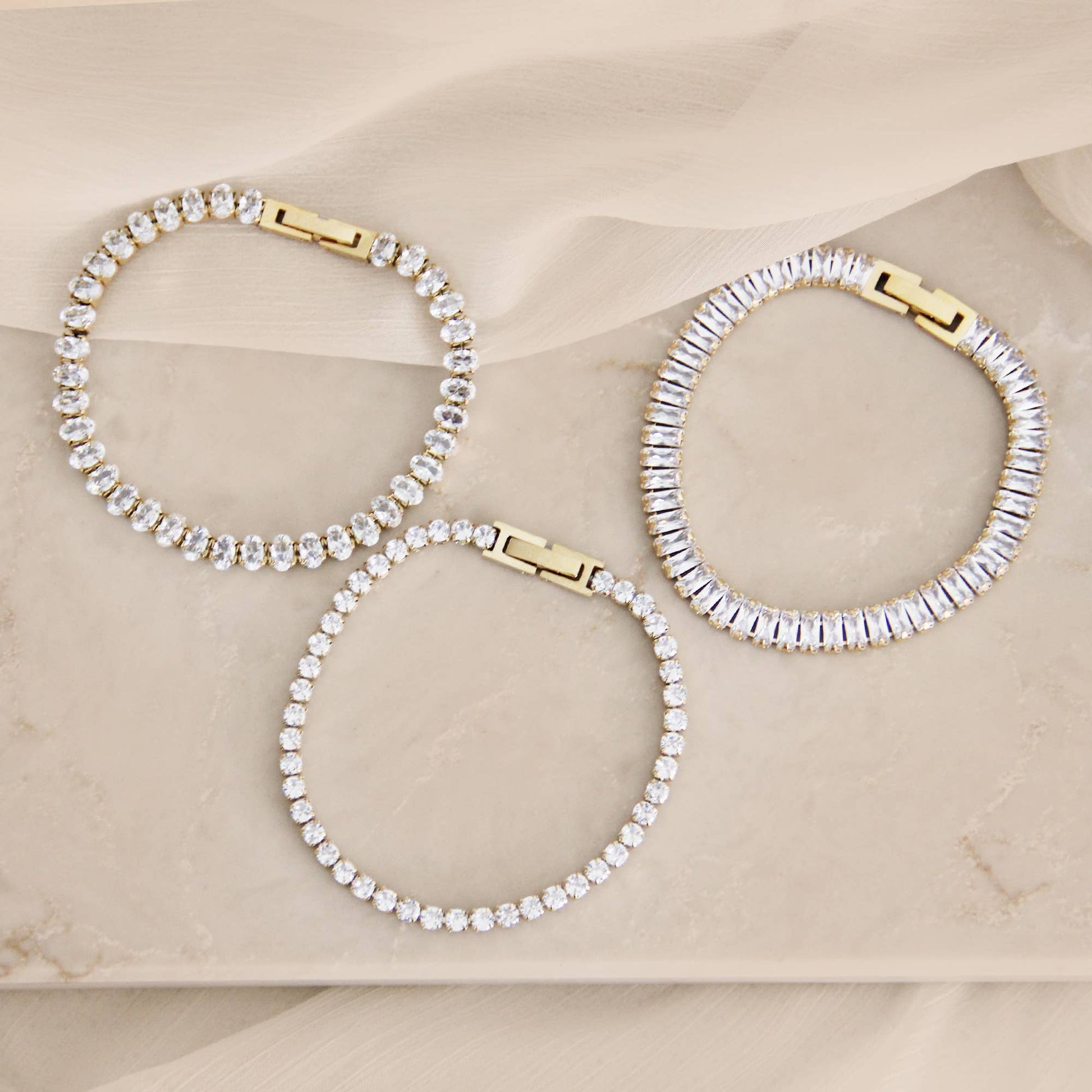 Minimal CZ tennis bracelet in gold over surgical steel, featuring a refined, understated design styled on a neutral marble surface.