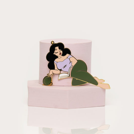 Enamel bookamark of a woman lying on a book with green pants a white background