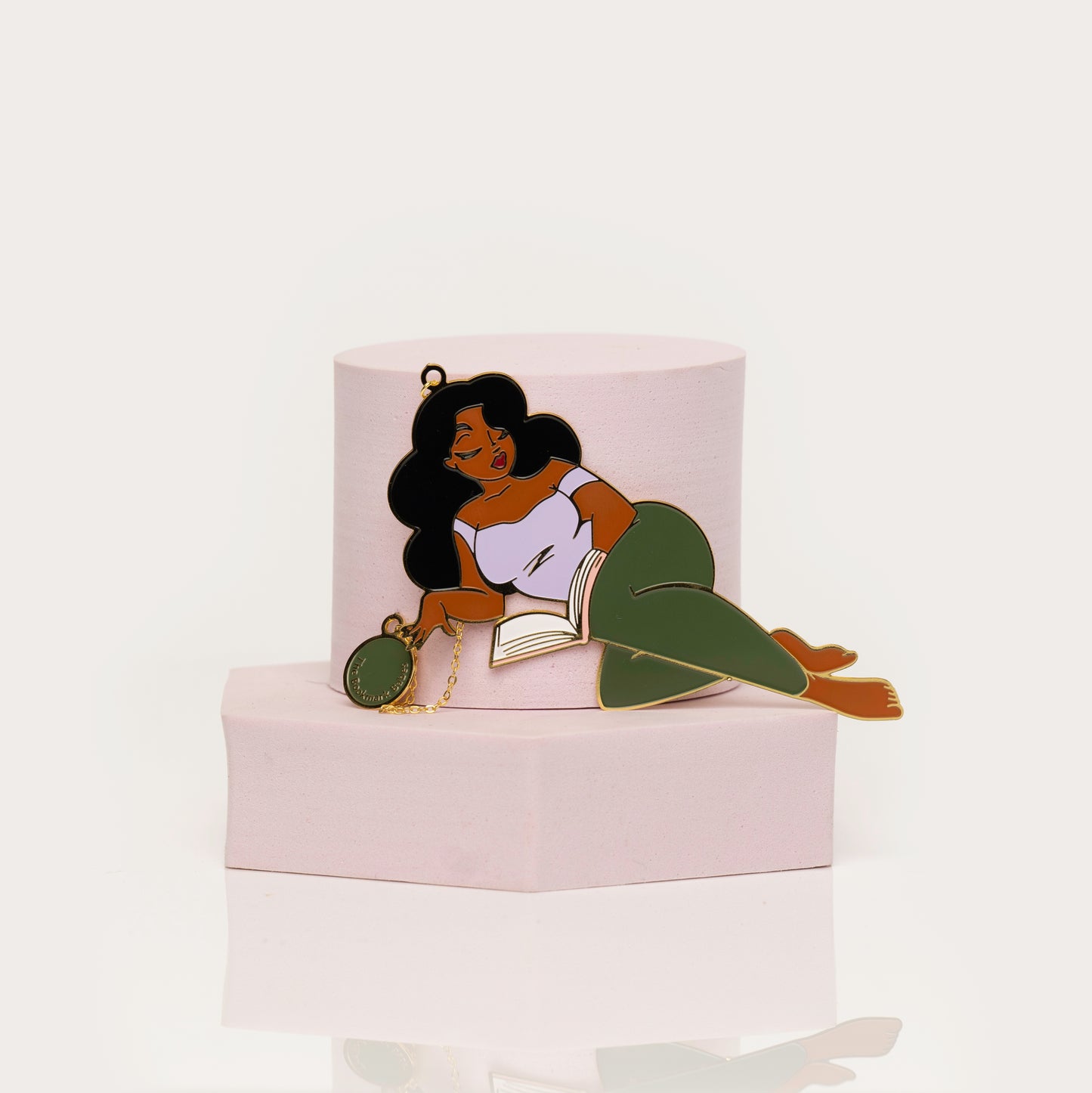 Enamel bookamark of a woman lying on a book with green pants a white background