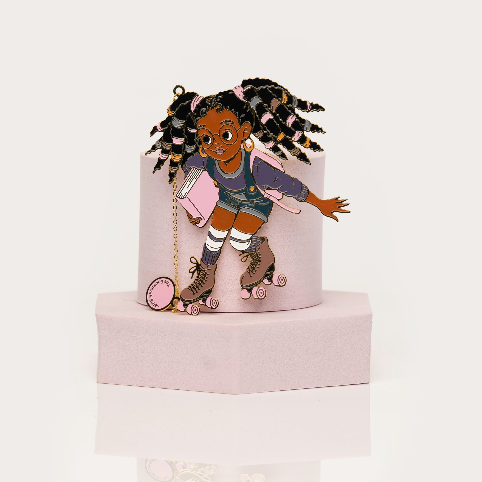 Enamel bookmark of Black girl on rollerskates  with locs holding a book
