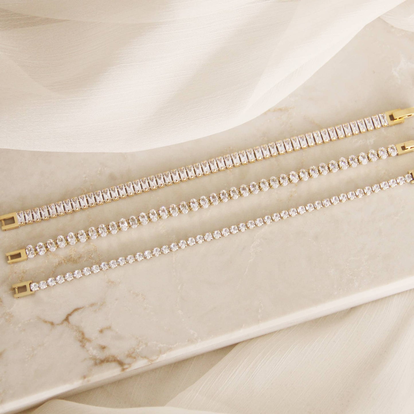 Minimal CZ tennis bracelet in gold over surgical steel, featuring a refined, understated design styled on a neutral marble surface.
