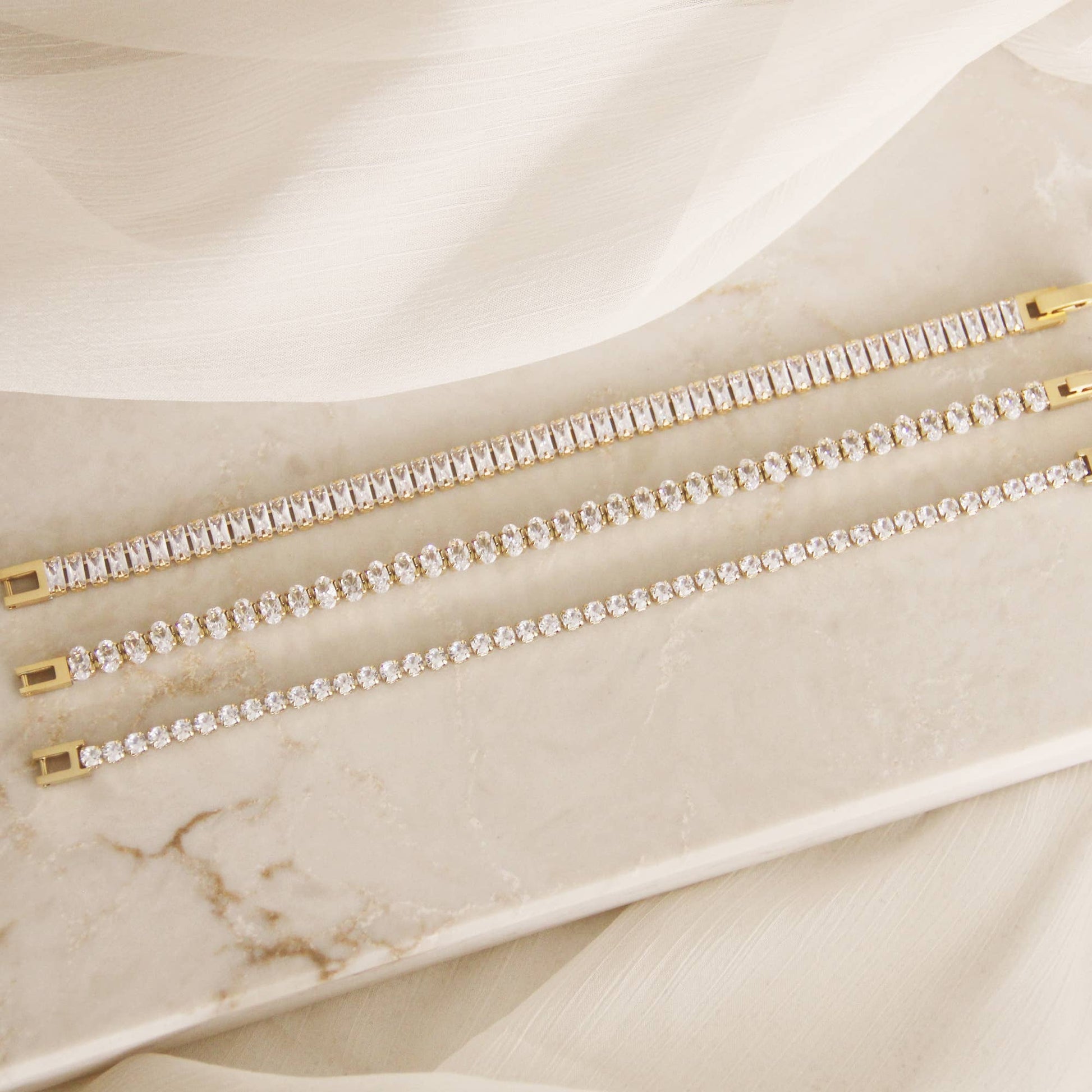 Minimal CZ tennis bracelet in gold over surgical steel, featuring a refined, understated design styled on a neutral marble surface.