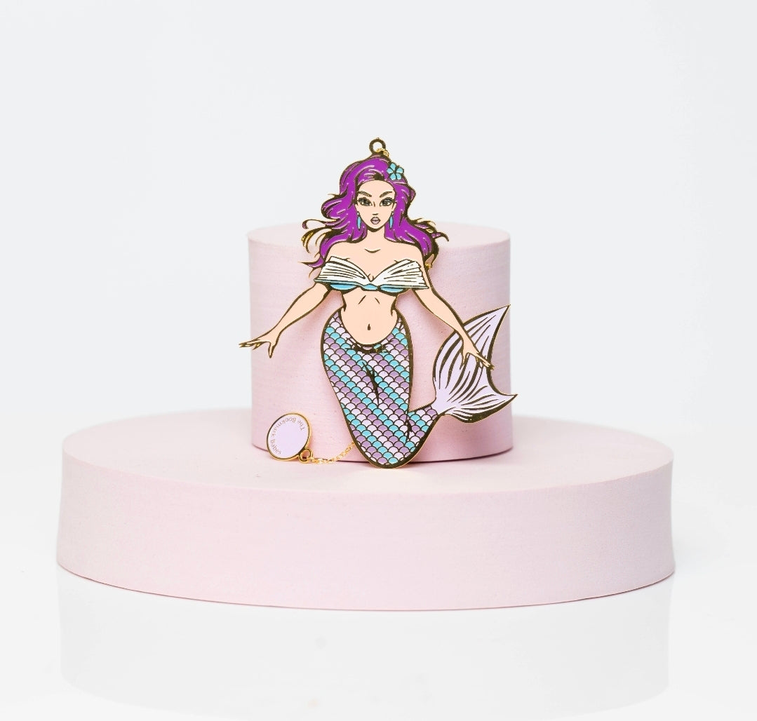 Enamel mermaid bookmark with flowing lavender hair, shimmering blue tail, and gold detailing; Naiya Pearl is posed mid-swim with a confident gaze.