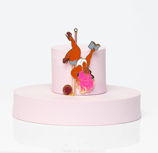 Enamel bookmark featuring Boudoir Bambi, a pink-haired pole-dancing pin-up babe reading a book mid-spin. Styled with gold accents, white leotard, and high heels, displayed on a soft blush pedestal.