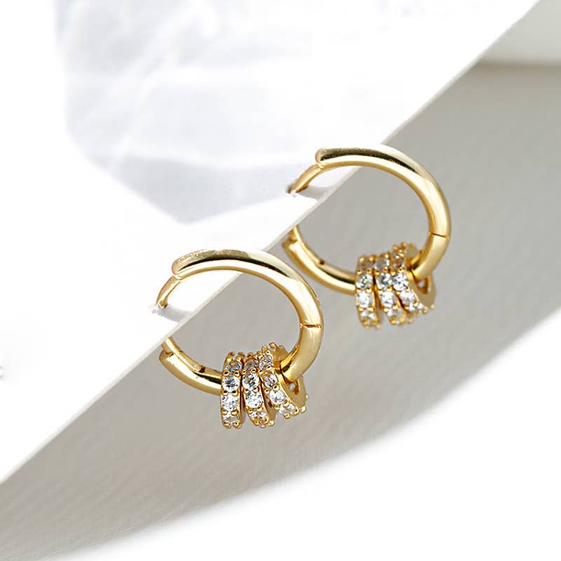 Gold CZ huggie hoop earrings with small cubic zirconia accents, styled on a neutral surface with a minimal aesthetic.