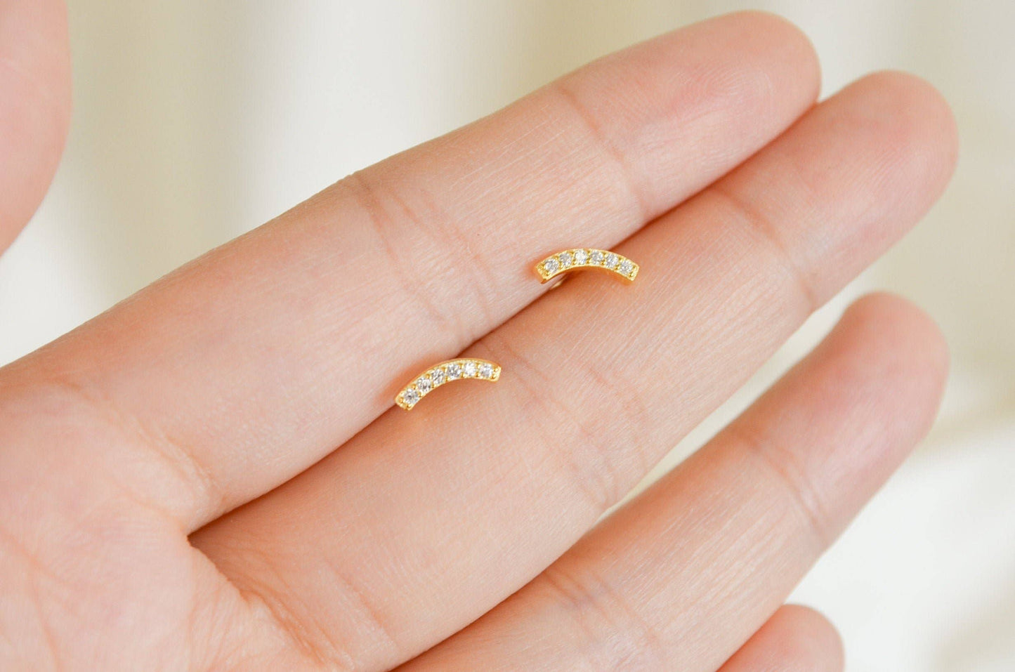 Tiny gold bar stud earrings in gold vermeil, worn on ear with a minimal, understated jewelry aesthetic.