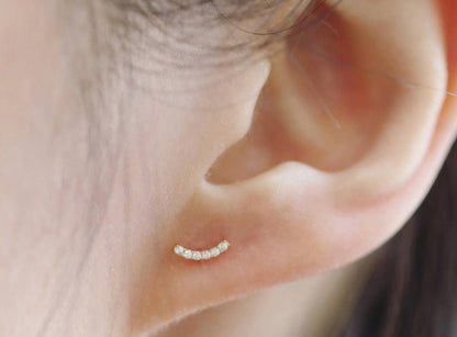 Tiny gold bar stud earrings in gold vermeil, worn on ear with a minimal, understated jewelry aesthetic.